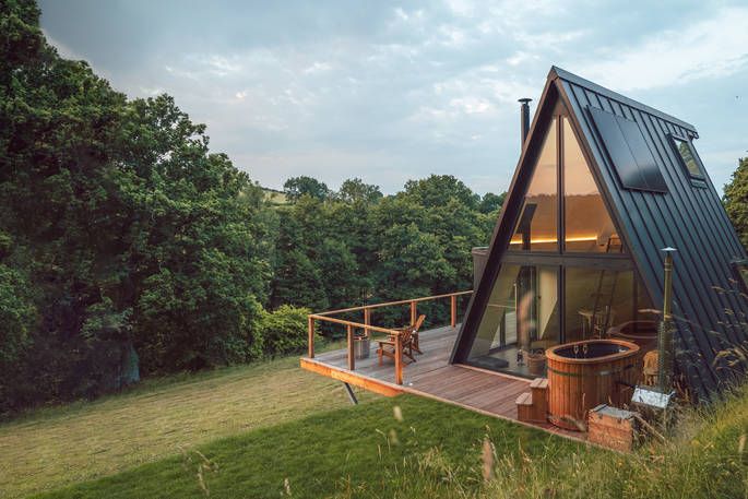 A Frame cabin in field with large glass window and hot tub on decking 