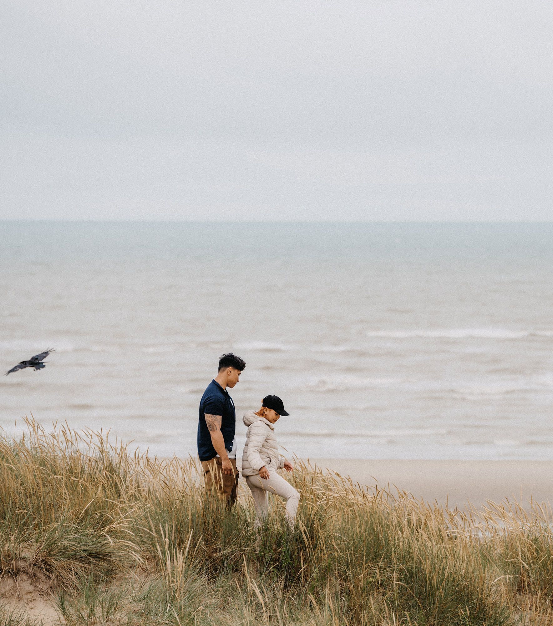 Two people walking over sand dunes at the beach 