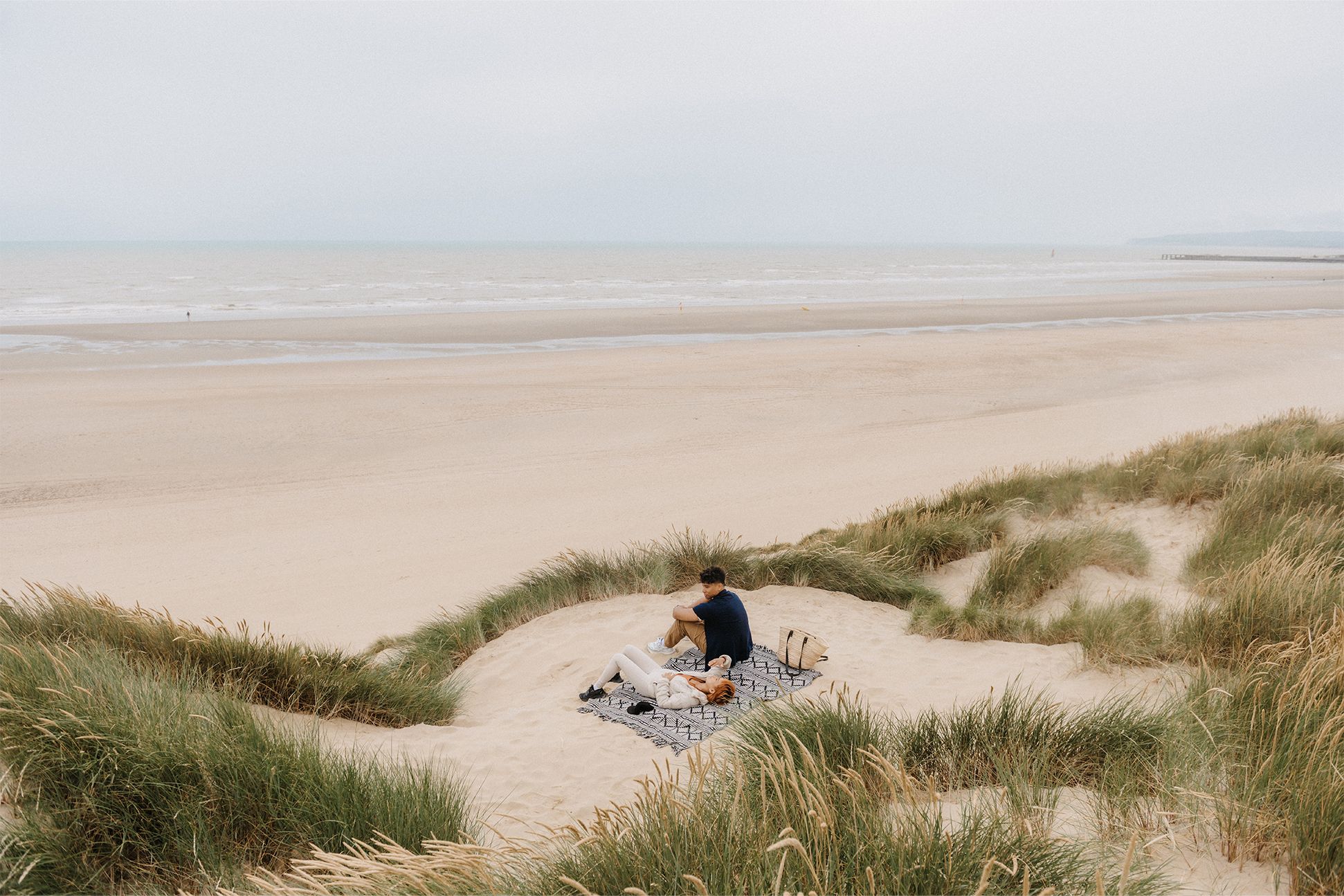 A male and female couple relaxing on the beach sand dunes with a view of the sea 