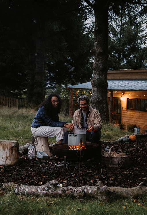 Two people cooking with a large pot on a campfire 